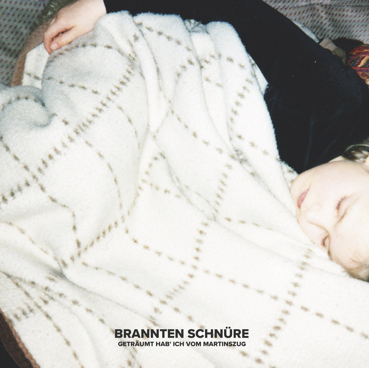 Person wrapped in a white textured blanket with text 'BRANNTEN SCHNURRE' at the bottom.