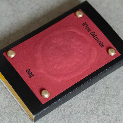 Close-up of a red-on black cassette case with gold rivets on a gray surface