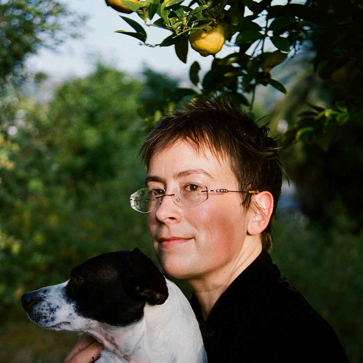 Person holding a dog with a lemon tree in the background